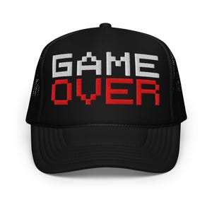 May include: Black trucker hat with the words "GAME OVER" embroidered in white and red pixelated font. The hat has a mesh back and a curved brim. A fun accessory for gamers.