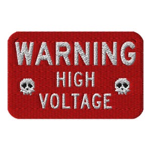 Puede incluir: Parche rojo bordado con las palabras "WARNING HIGH VOLTAGE" en hilo blanco. Dos pequeños símbolos de calavera y huesos cruzados flanquean el texto. El parche tiene forma rectangular con esquinas redondeadas.