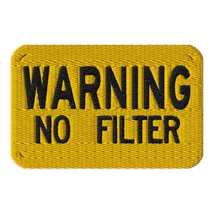 May include: Embroidered yellow patch with the words "WARNING NO FILTER" in black thread. The patch has a rectangular shape with rounded corners and a textured appearance, suggesting a fabric material.