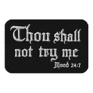 Può includere: Una toppa rettangolare ricamata nera con testo bianco che recita "Thou shall not try me" in un carattere gotico stilizzato, con il testo aggiuntivo "Mood 24:7" posizionato nell'angolo in basso a destra in un carattere più piccolo.