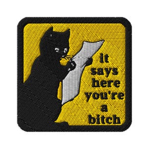Puede incluir: Parche bordado con un gato negro leyendo un pergamino. El parche tiene un fondo amarillo y el texto "It says here you're a bitch" en negro. El parche tiene un borde negro.