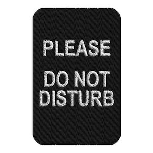 May include: A rectangular black embroidered patch with rounded corners featuring the white stitched text PLEASE DO NOT DISTURB in three lines. The embroidery has a visible vertical thread texture throughout the black background and white lettering.