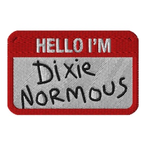 Könnte beinhalten: Ein rechteckiger gestickter Aufnäher mit rotem Rand und weißer Mitte. Der obere Bereich enthält den weißen Sticktext HELLO I'M. Der untere Bereich zeigt den schwarzen Sticktext Dixie NORM OUS in einem handschriftlichen Stil.