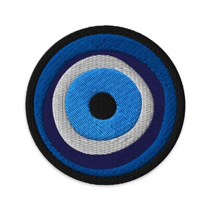 May include: Embroidered patch featuring a stylized eye design. The patch has concentric circles in shades of blue, white, and black, with a black center. The outer border is black. The design is circular and appears to be made of fabric.