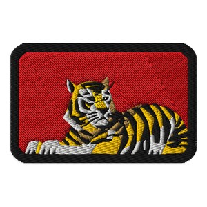 May include: Embroidered patch featuring a tiger with yellow and black stripes, white accents, and a red background. The patch has a black border and is rectangular with rounded corners.