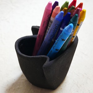Peut inclure: Un récipient noir en forme de cœur rempli de crayons de couleur. Les crayons sont de différentes nuances de rose, violet, bleu, vert et jaune. Le récipient est fait d'un matériau texturé.