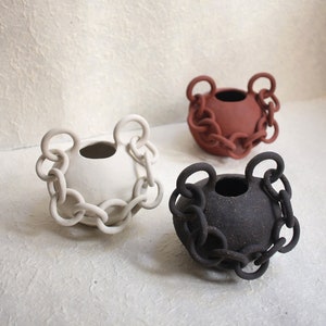 Puede incluir: Tres jarrones de cerámica con un diseño de cadena. Los jarrones son de color blanco, marrón y negro.