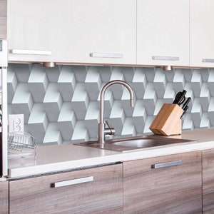 Può includere: Una cucina moderna con armadi bianchi, un forno in acciaio inossidabile e un paraschizzi in piastrelle geometriche grigio e bianco. Un lavello in acciaio inossidabile con un rubinetto cromato è al centro del piano di lavoro. Un portacoltelli in legno con coltelli neri è sul piano di lavoro.