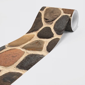 Puede incluir: Un rollo de papel pintado decorativo con un patrón de piedras. El diseño incluye piedras de varios tonos marrones, grises y beige, separadas por lechada blanquecina. El papel pintado está parcialmente desenrollado.