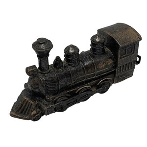 May include: A detailed, antique-style miniature train model in a dark bronze color. The locomotive features a classic design with a smokestack, a rounded engine, and a small cabin at the rear. The model is made of metal and has intricate detailing.
