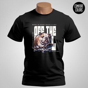 以下が含まれることがあります： スケートボードに乗ったブルドッグが描かれた黒いTシャツ。「OFF THE WALL」の文字入り。デザインには「WHEN IN DOUBT SKATE IT OUT」と「SKATE OUT OF THE BOX」のフレーズが含まれています。シャツにはComfort Colorsのラベルが付いています。