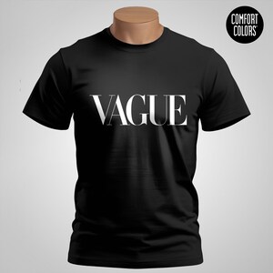 Pode incluir: Camiseta preta com a palavra "VAGUE" em branco, com texto estilizado no peito. A camiseta é exibida em um manequim. Um logotipo circular com as palavras "COMFORT COLORS" está no canto superior direito.