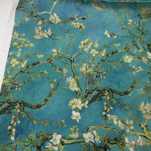 Op de afbeelding: Stof met een schilderij van bloeiende amandelboomtakken tegen een turquoise blauwe achtergrond. Het kunstwerk heeft een textuur, met zichtbare penseelstreken en een palet van blauw, groen en wit. Geschikt voor diverse knutselprojecten.
