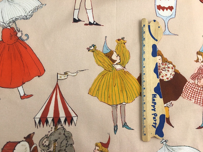 May include: A pink fabric with a repeating pattern of girls in various dresses, a circus tent, and a wooden ruler with the words "Happy Party" printed on it.