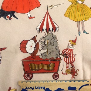 May include: A whimsical fabric print featuring a red, white, and blue striped circus tent with a gray elephant, a red and white striped clown, a brown bear playing a drum, and a monkey. The background is a light beige with other figures in red, yellow, and blue.