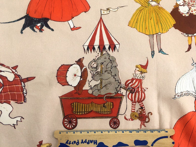 May include: A whimsical fabric print featuring a red, white, and blue striped circus tent with a gray elephant, a red and white striped clown, a brown bear playing a drum, and a monkey. The background is a light beige with other figures in red, yellow, and blue.