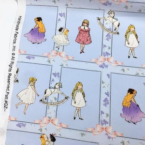 Pode incluir: Tecido azul claro com um padr&atilde;o repetido de meninas ilustradas em vestidos, algumas com cabelos longos e loiros, e cavalos de baloi&ccedil;o. La&ccedil;os cor-de-rosa e detalhes florais decoram o fundo. O texto "Handmade Fabrics, Inc. &copy; All Rights Reserved. Patt.#GZ--" est&aacute; impresso &agrave; esquerda.