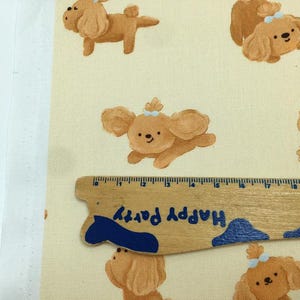 May include: Fabric featuring a repeating pattern of cartoon poodle dogs in shades of brown, with blue bows. A wooden ruler with the text "Happy Party" is placed on the fabric. The fabric has a cream-colored background.