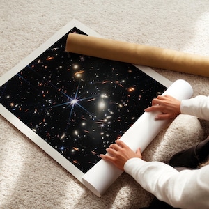 A person is holding a roll of paper and unfolding a poster of a distant galaxy, which is displayed on the floor.
