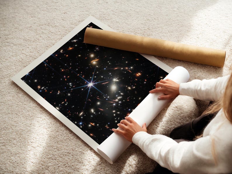 A person is holding a roll of paper and unfolding a poster of a distant galaxy, which is displayed on the floor.
