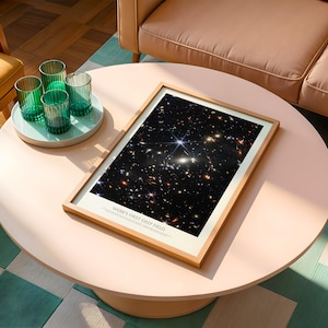 a framed picture of a starry night sky on a white coffee table, with a tray of green glasses and a brown couch in the background.
