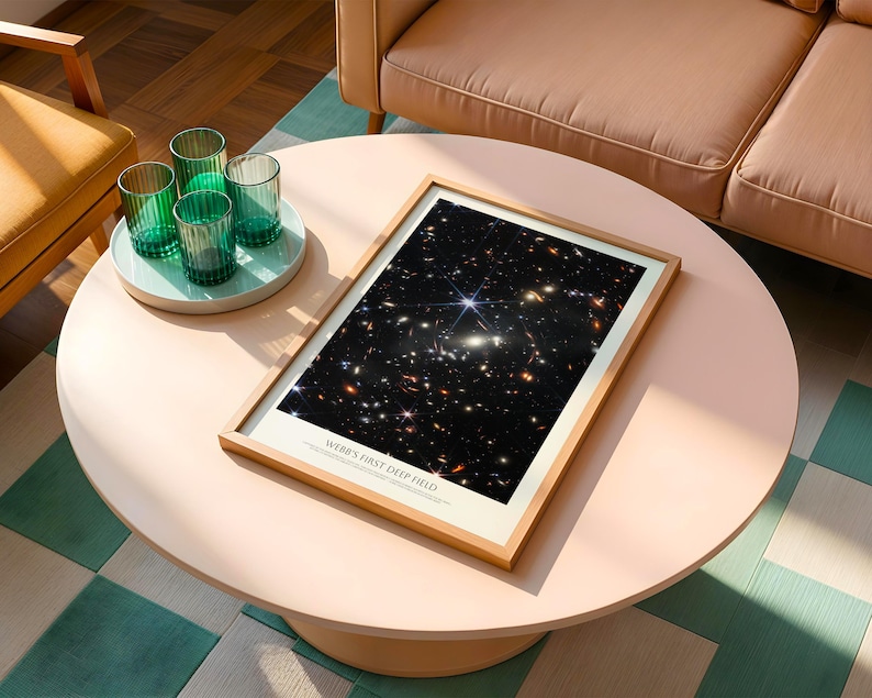 a framed picture of a starry night sky on a white coffee table, with a tray of green glasses and a brown couch in the background.