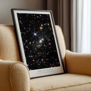 a framed photograph of a distant galaxy, with the text "WEB'S FIRST DEEP FIELD" below the image.