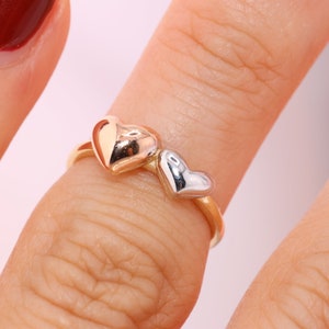 May include: A gold ring with two heart-shaped charms. The larger charm is gold and the smaller charm is silver.
