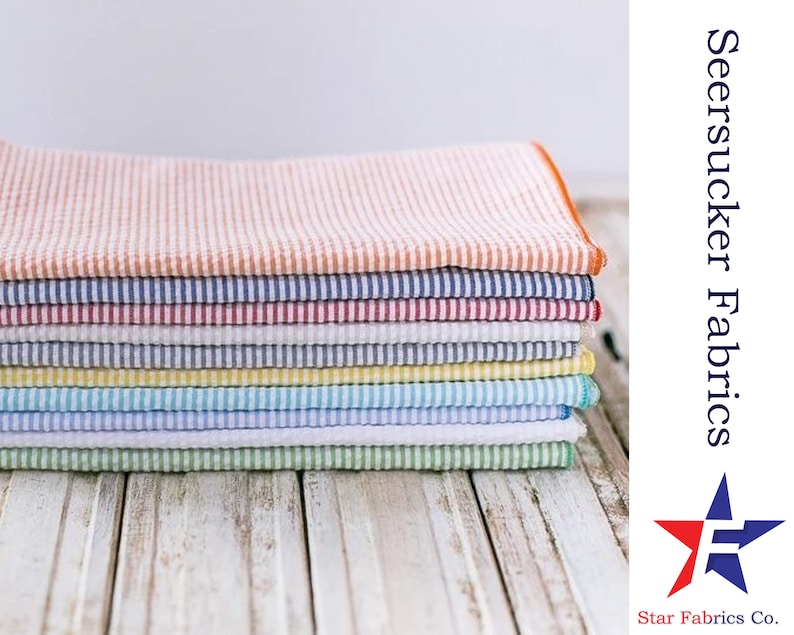 May include: A stack of colorful seersucker fabrics in various stripes. The fabrics are folded neatly and arranged on a white wooden surface. The text "Seersucker Fabrics" and "Star Fabrics Co." is visible in the image.