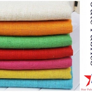 May include: A stack of seven different colored burlap fabrics. The fabrics are in the following order from top to bottom: white, orange, green, red, pink, yellow, and blue. The fabrics are all folded in half and stacked on top of each other. The text "Jute Fabrics" and "Star Fabrics Co." is visible in the image.