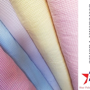 May include: Four rolls of seersucker fabric in pink, light blue, lavender, and yellow. The fabric has a small gingham pattern. The text "Seersucker Fabrics" and "Star Fabrics Co." is visible in the image.