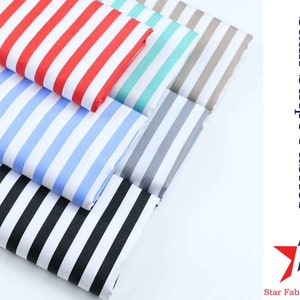 Op de afbeelding: Een stapel van vier verschillende gestreepte stoffen. De stoffen zijn allemaal van satijn en hebben een witte achtergrond met gekleurde strepen. De kleuren zijn rood, blauw, turquoise en grijs. De stoffen zijn gelabeld met "Satin Stripe Fabrics" en "Star Fabrics Co."