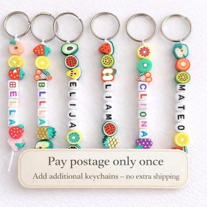 Könnte beinhalten: Ein Set aus drei Keramikbechern mit gesprenkelter, cremefarbener Glasur. Jeder Becher zeigt ein handgemaltes Design: ein blau-grünes Blatt, eine gelbe Blume und eine rote Beere. Die Becher haben eine einfache, abgerundete Form.