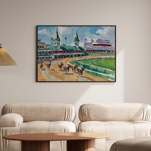 Puede incluir: Una pintura enmarcada representa una carrera de caballos en un hip&oacute;dromo. La obra presenta caballos con jinetes, un campo interior verde y gradas bajo un cielo azul. La pintura est&aacute; en un marco negro y cuelga de una pared beige.