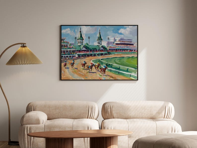 Puede incluir: Una pintura enmarcada representa una carrera de caballos en un hip&oacute;dromo. La obra presenta caballos con jinetes, un campo interior verde y gradas bajo un cielo azul. La pintura est&aacute; en un marco negro y cuelga de una pared beige.