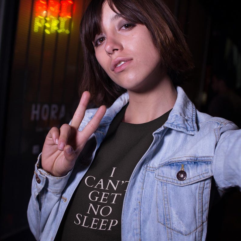 Black unisex tee with large white text saying “I Can’t Get No Sleep” on a plain background, insomnia quote tee, music‑inspired slogan top.