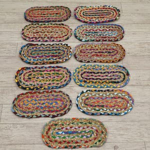 Puede incluir: Diez alfombras ovaladas trenzadas en varios colores, incluyendo rojo, azul, verde y amarillo. Las alfombras están dispuestas sobre un suelo de madera clara, mostrando sus intrincados patrones y texturas tejidas.