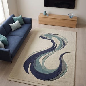May include: A rectangular area rug featuring a cream-coloured base with a large, abstract, swirling design in shades of navy blue, teal, and light blue. The rug has a textured, layered appearance with curved, flowing shapes that create a dynamic pattern.