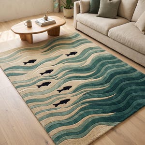 Peut inclure: Un tapis rectangulaire présentant un motif ondulé texturé dans des tons beige, vert clair et bleu sarcelle foncé. Le design comprend plusieurs petites silhouettes de poissons noires unies nageant sur la surface multicouche.