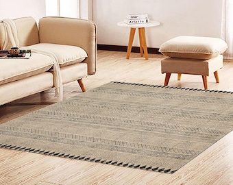 May include: A beige and gray area rug with a geometric pattern and a fringe border. The rug is laid out on a hardwood floor in a living room setting.