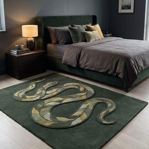 Puede incluir: Una alfombra rectangular de color verde bosque profundo que presenta un gran motivo de serpiente central. La serpiente está representada en un patrón texturizado y superpuesto de tonos oliva, salvia y amarillo mostaza, con un borde en relieve.