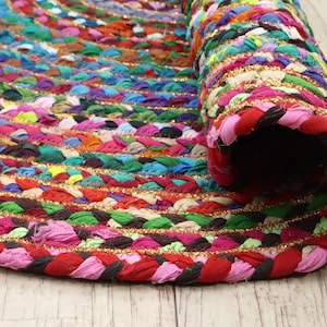 Może przedstawiać: Zwinięty, wielokolorowy, pleciony dywan. Dywan ma żywą mieszankę kolorów, w tym czerwony, różowy, zielony, niebieski i złoty. Widoczny jest pleciony wzór, a dywan jest częściowo zwinięty.