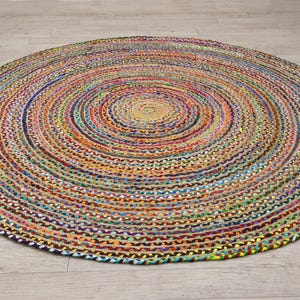 Könnte beinhalten: Ein runder, mehrfarbiger geflochtener Teppich. Der Teppich weist konzentrische Kreise in verschiedenen Farben auf, darunter Blau, Orange, Gelb, Grün und Lila. Der Teppich besteht aus einem gewebten Material und ist für den Innenbereich geeignet.