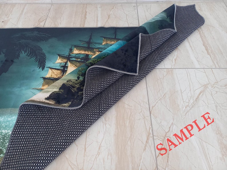 May include: A rolled-up rug featuring a detailed illustration of a tall ship sailing on the ocean. The design includes a palm tree, rocky cliffs, and a dark blue sky. The rug's underside is black with a white dotted pattern. The word "SAMPLE" is printed in red.