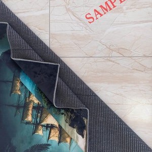 May include: A rolled-up area rug featuring a detailed illustration of a tall ship sailing on a dark, misty sea. The rug's design includes a palm tree and rocky cliffs. The word "SAMPLE" is printed in red on the background.