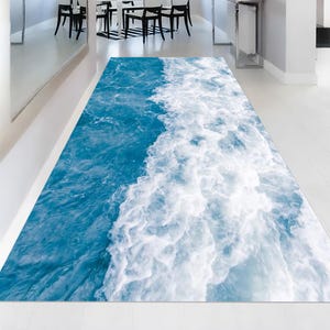 May include: A rectangular rug with a vibrant ocean wave design. The rug features shades of blue and white, creating a realistic depiction of water movement. The design is detailed and appears to be digitally printed.