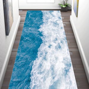 May include: A rectangular runner rug with a vibrant ocean wave design. The rug features shades of blue and white, mimicking the foamy crest of a wave. The rug is placed on a wooden floor in a hallway.