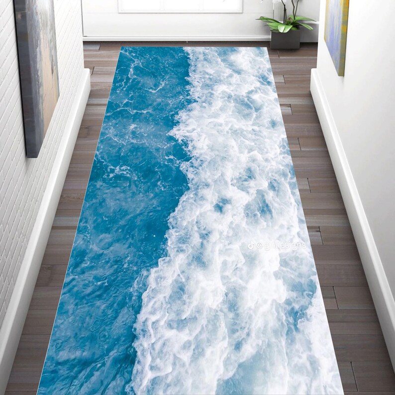 May include: A rectangular runner rug with a vibrant ocean wave design. The rug features shades of blue and white, mimicking the foamy crest of a wave. The rug is placed on a wooden floor in a hallway.