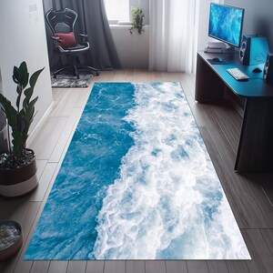 May include: A rectangular rug featuring a vibrant ocean wave design. The rug showcases a dynamic blend of deep blue and white, creating a realistic water effect. The rug is placed on a wooden floor.