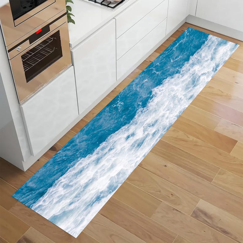 May include: A long, rectangular kitchen rug with a vibrant ocean wave design. The rug features a dynamic pattern of white foamy waves against a deep blue background. The rug is placed on a wooden floor, adding a touch of coastal decor.